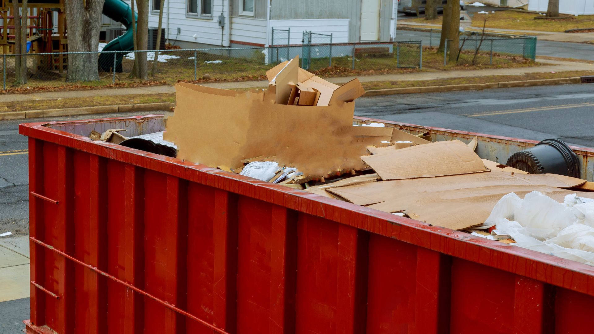 Red dumpster filled with cardboard boxes and debris on urban street